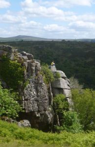 A person perched on a massive rock, with a view over green countryside and hills.